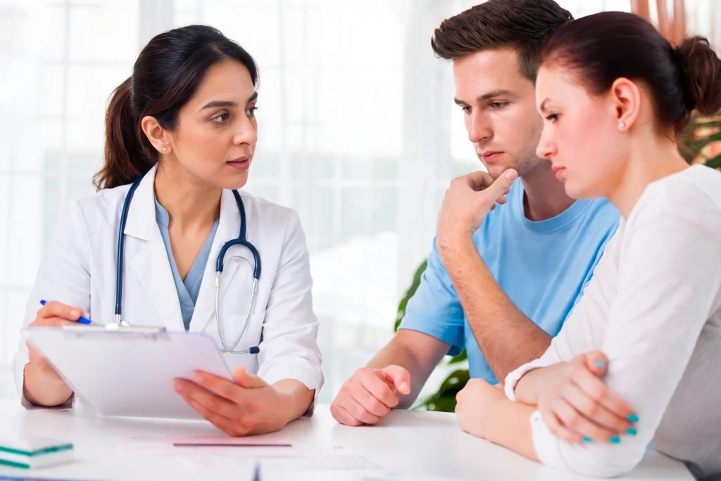 Female doctor holding a clipboard while consulting with a young couple at a no insurance medical clinic.