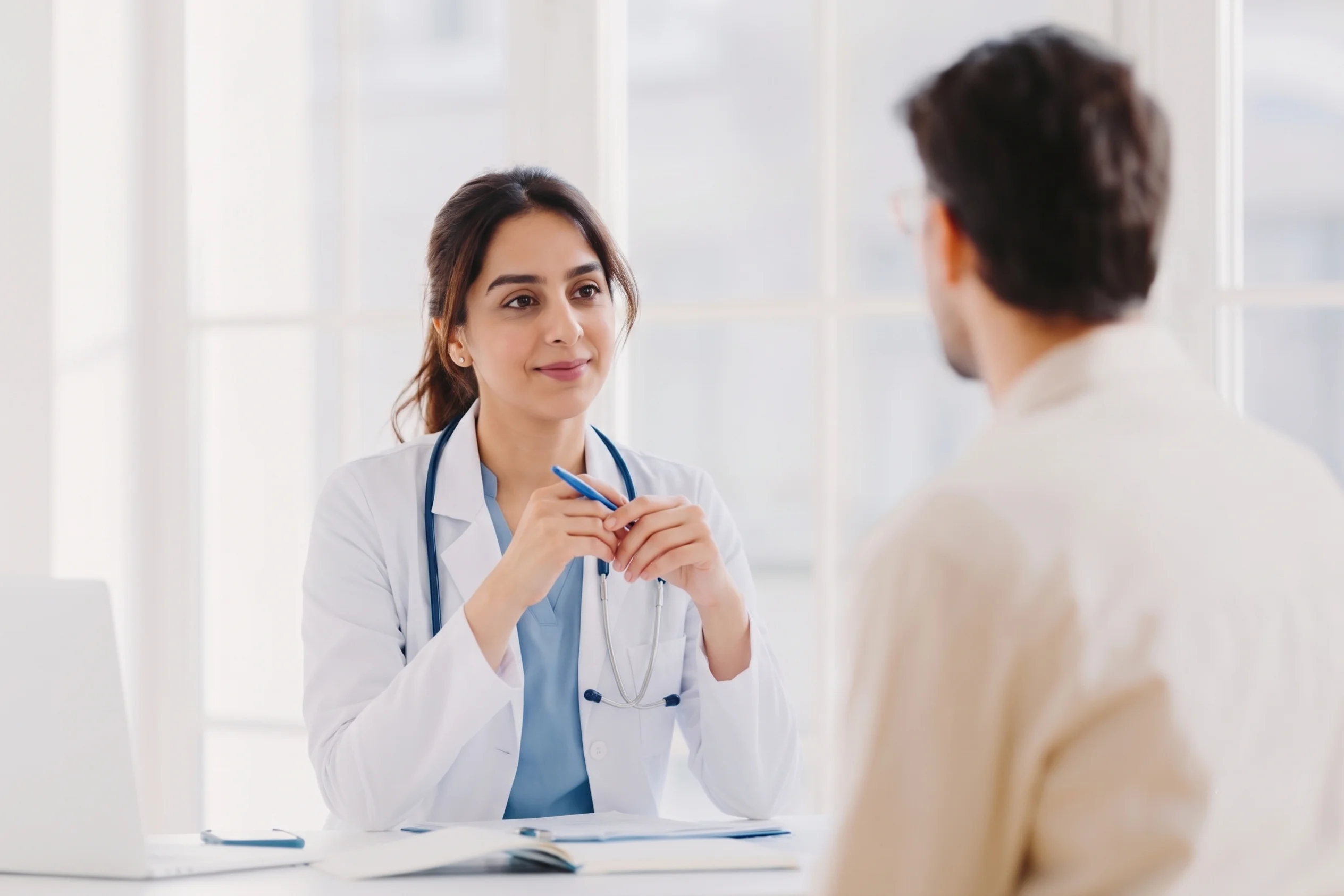 Female doctor sitting at her desk and listening to a patient at a no insurance medical clinic.