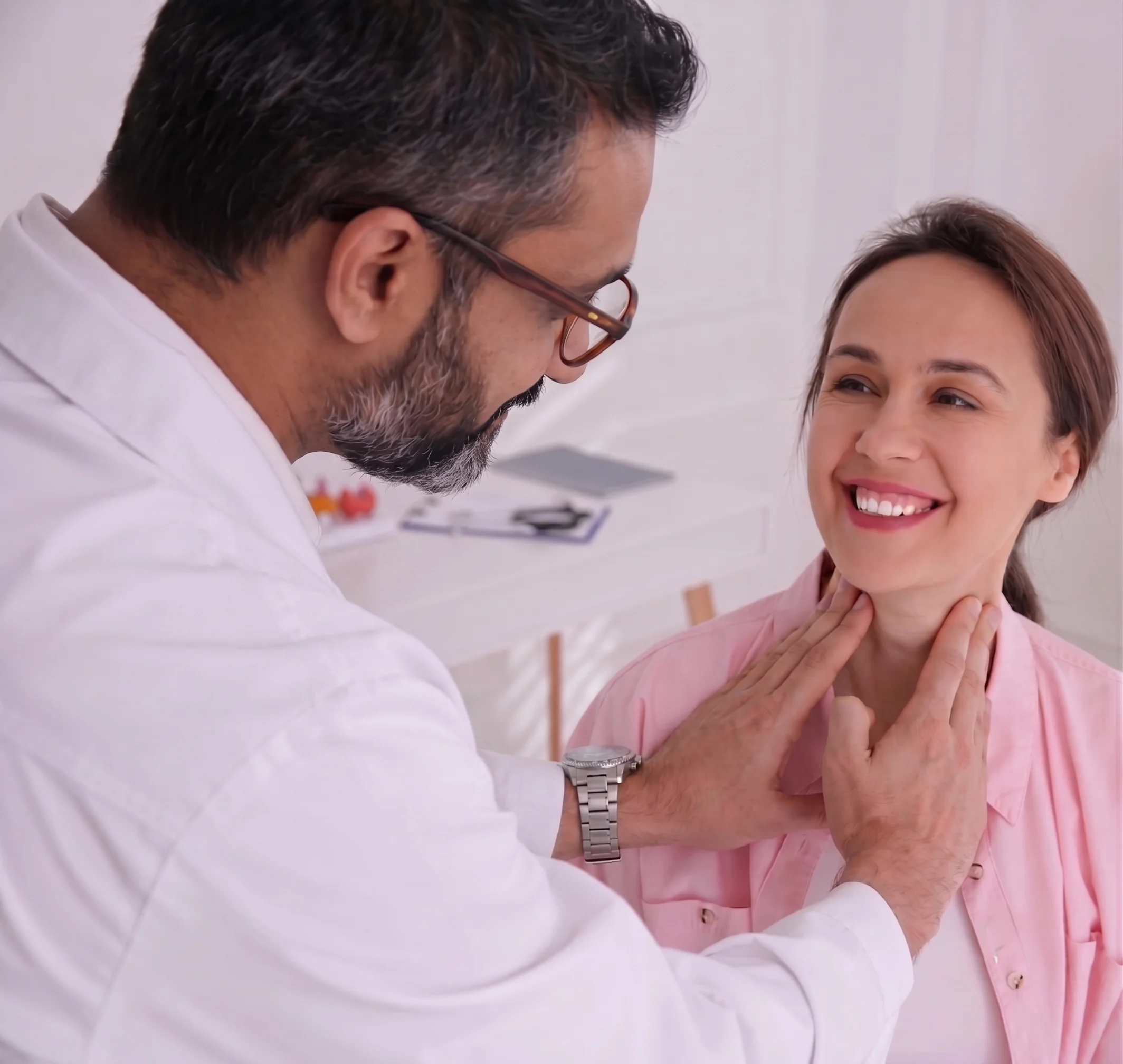 Male doctor checking a smiling woman's neck and thyroid during an exam at a no insurance medical clinic.