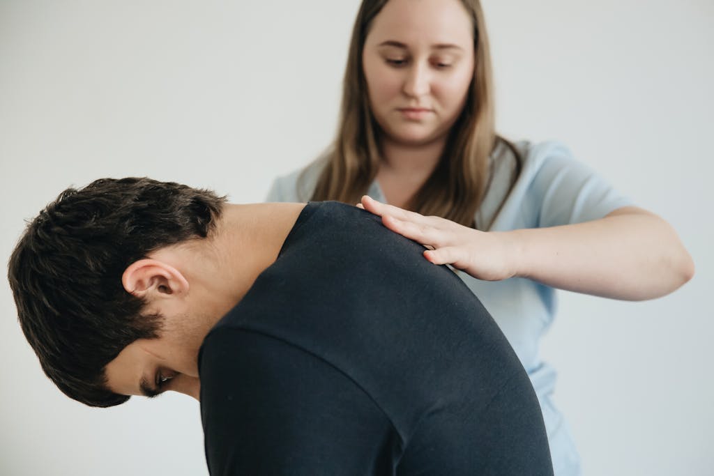 A physiotherapist assisting a patient with back pain in an indoor clinic setting.