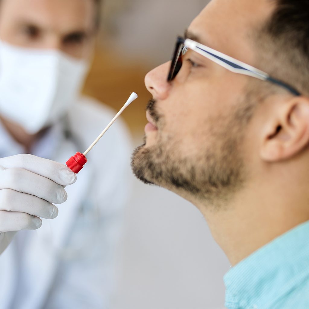 A medical professional in a face shield performs a throat swab for rapid tests in Houston to check for strep and flu.