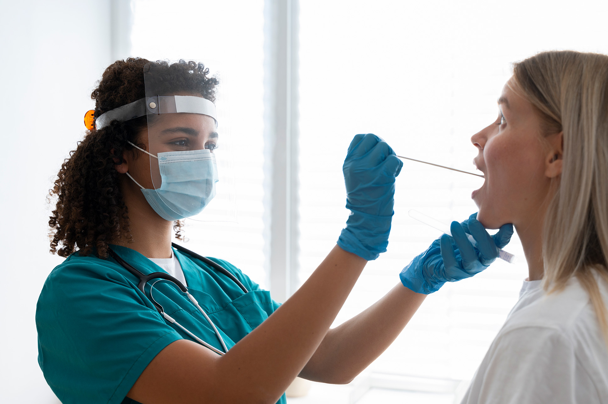 A healthcare worker in protective gear performs a throat swab as part of routine on-site testing and procedures.