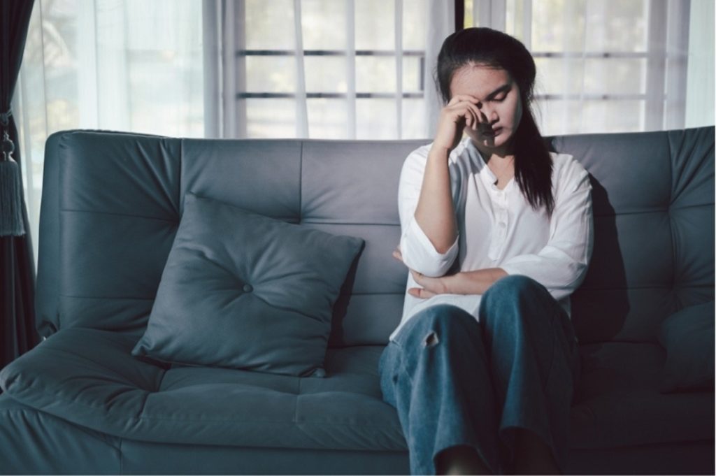 Distressed woman on sofa needing professional psychiatry consultations care in Houston, TX for mood disorder support.